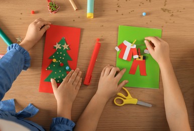 Little children making beautiful Christmas greeting cards at wooden table, top view