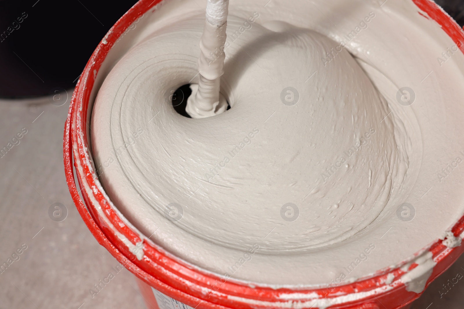 Photo of Mixing putty with electric mixer in red bucket indoors, closeup