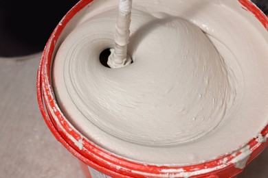 Photo of Mixing putty with electric mixer in red bucket indoors, closeup