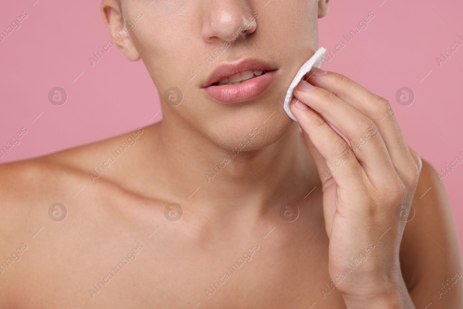 Photo of Man cleaning face with cotton pad on pink background, closeup