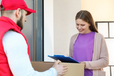 Photo of Woman receiving parcel from delivery service courier indoors