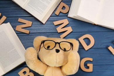 Photo of Dyslexia concept. Teddy bear, books and letters on blue wooden table, flat lay