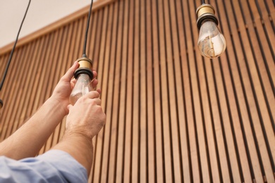 Man changing lamp light bulb indoors, closeup. Space for text