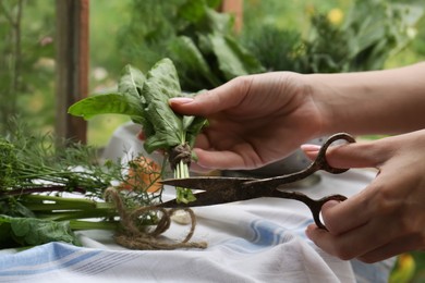 Photo of Woman cutting fresh green leaves with scissors indoors, closeup. Drying herbs