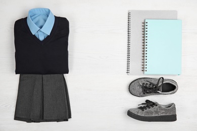 Photo of School uniform for girl and notebooks on white wooden background, top view