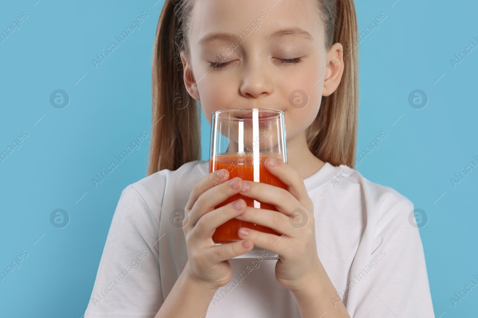 Photo of Little girl enjoying fresh juice on light blue background, closeup