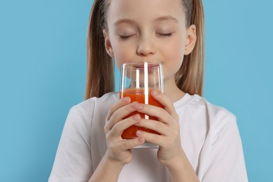 Photo of Little girl enjoying fresh juice on light blue background, closeup