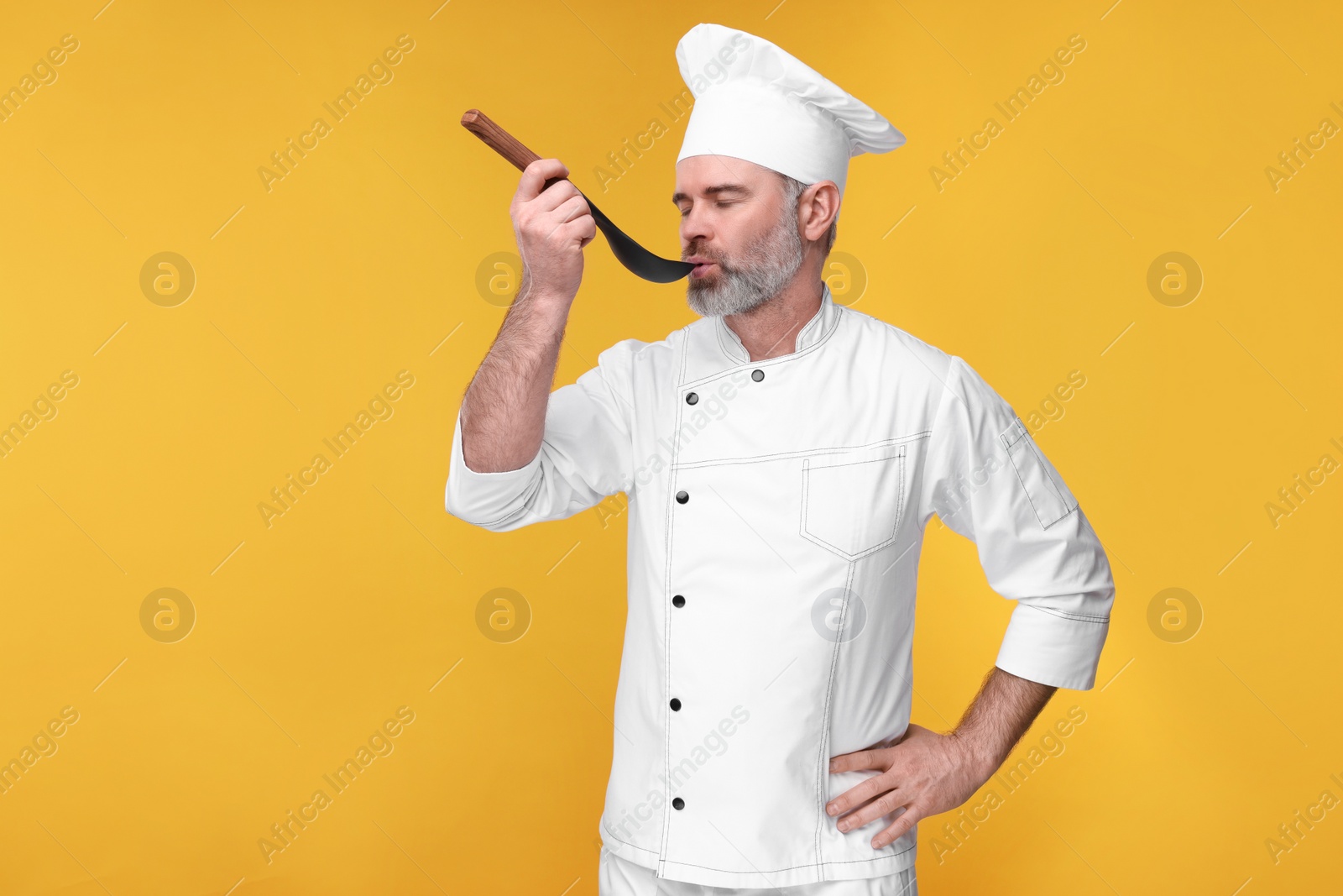 Photo of Chef in uniform tasting something on orange background