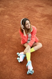 Photo of Happy stylish young woman with vintage roller skates and headphones sitting on tennis court