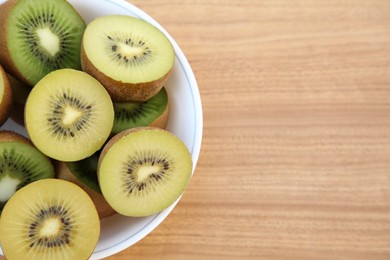 Photo of Bowl of many cut fresh kiwis on wooden table, top view. Space for text