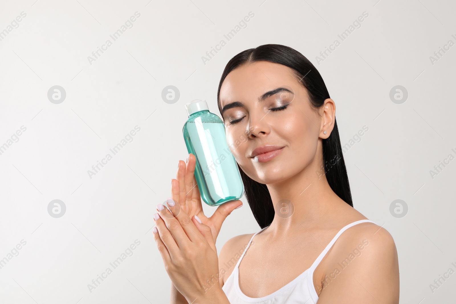 Photo of Young woman with micellar water on light grey background, space for text