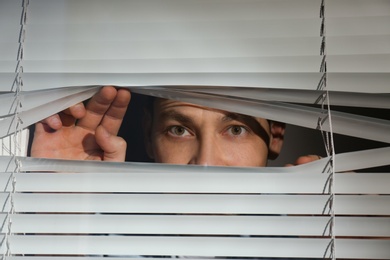 Curious man looking through Venetian window blinds