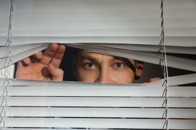 Photo of Curious man looking through Venetian window blinds