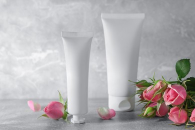 Photo of Tubes of hand cream and beautiful roses on light grey table
