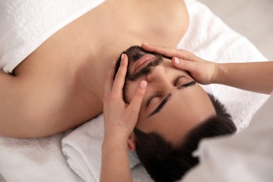 Photo of Young man receiving facial massage in beauty salon