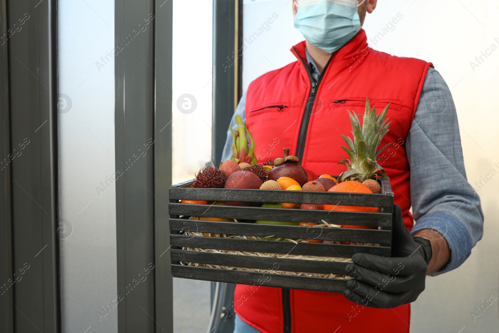 Photo of Courier holding crate with assortment of exotic fruits outdoors, closeup