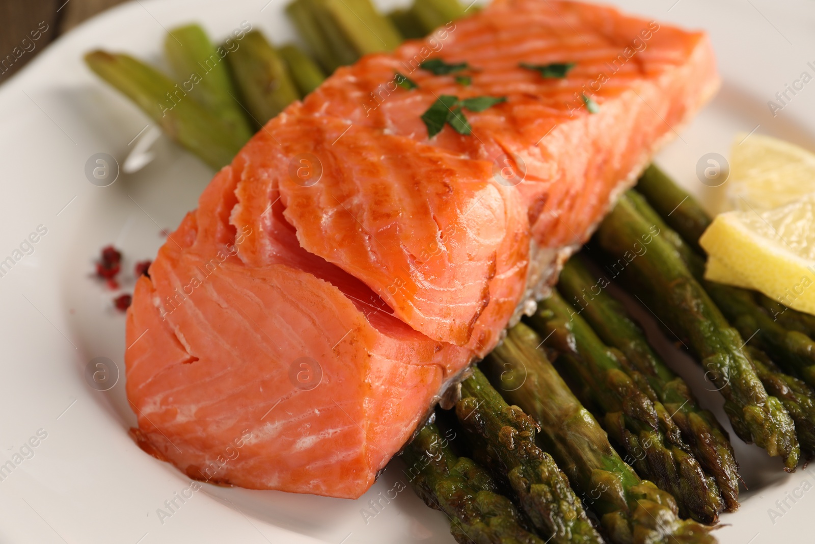 Photo of Plate with tasty grilled salmon, asparagus and lemon, closeup