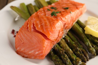 Photo of Plate with tasty grilled salmon, asparagus and lemon, closeup