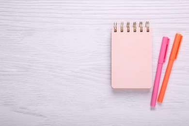 Notebook and colorful markers on white wooden background, flat lay. Space for text