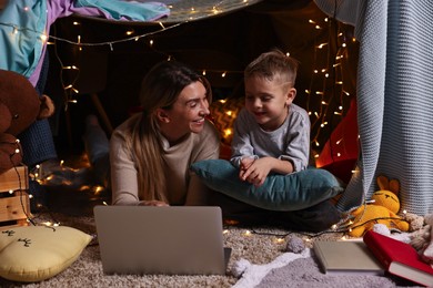Mother and her son with laptop in play tent at home
