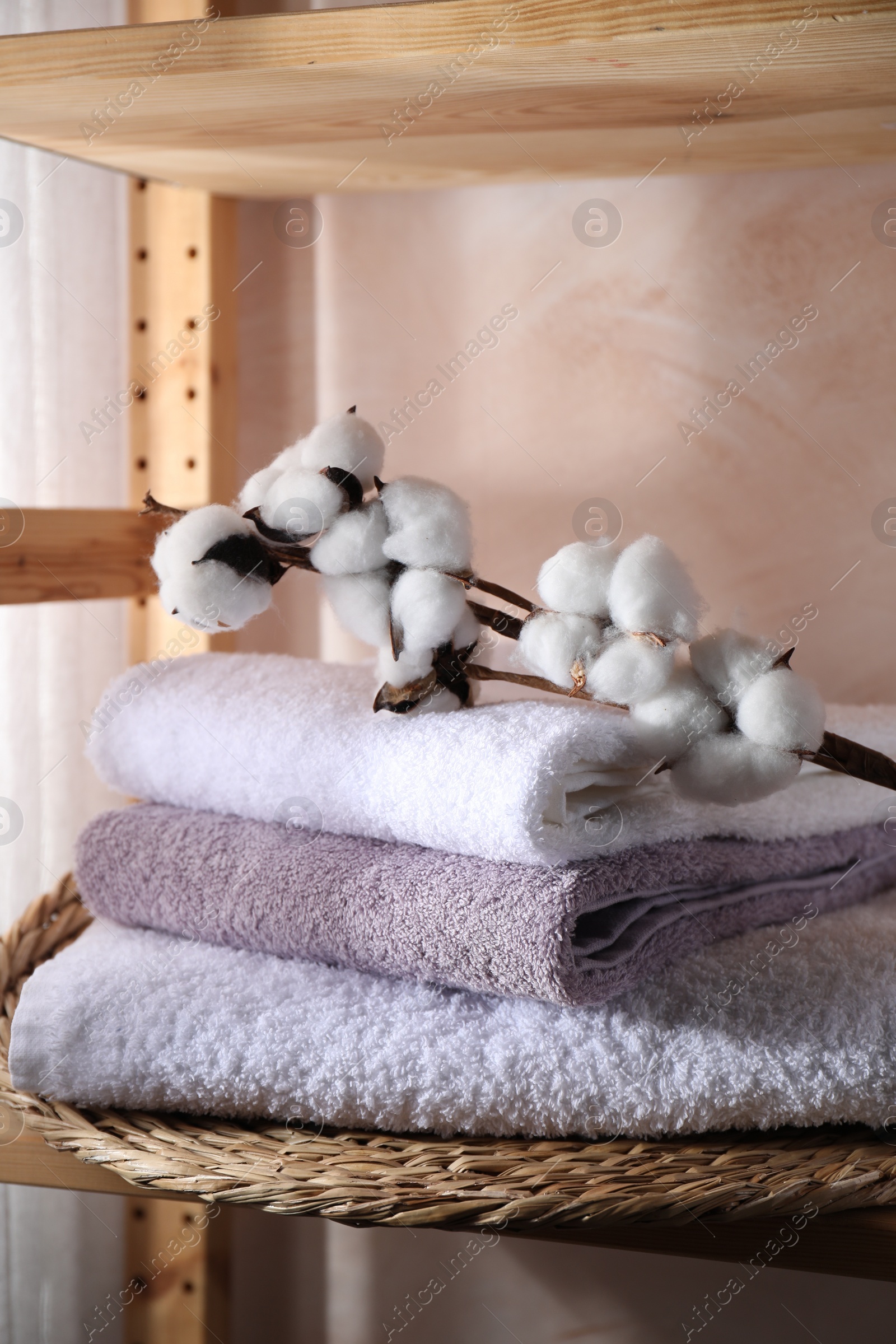 Photo of Stacked soft towels and cotton branch on shelf indoors