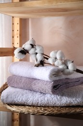 Photo of Stacked soft towels and cotton branch on shelf indoors