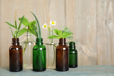 Glass bottles of different essential oils with plants on table