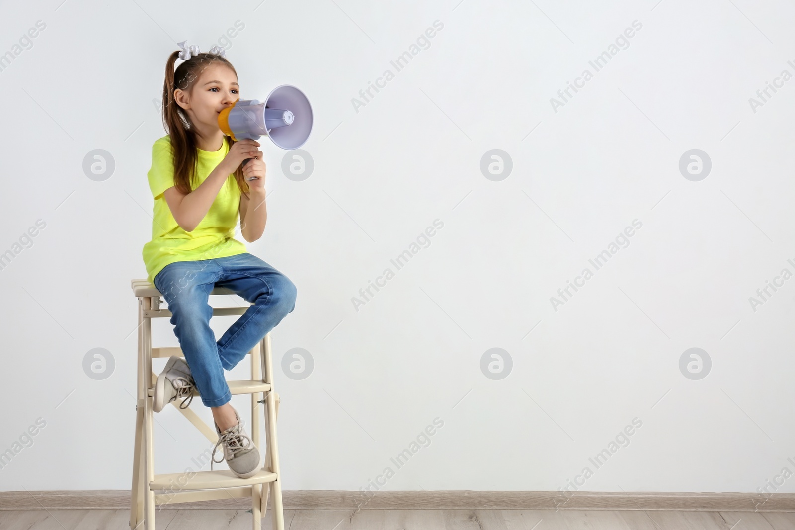 Photo of Cute little girl sitting with megaphone near white wall