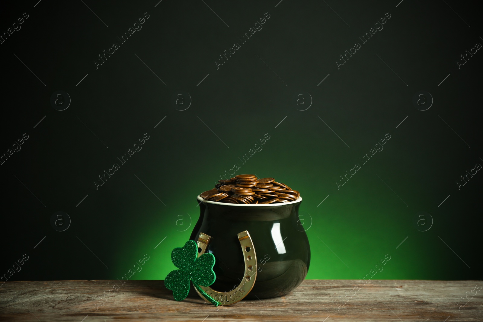 Photo of Pot with gold coins, horseshoe and clover on wooden table against dark background. St. Patrick's Day celebration