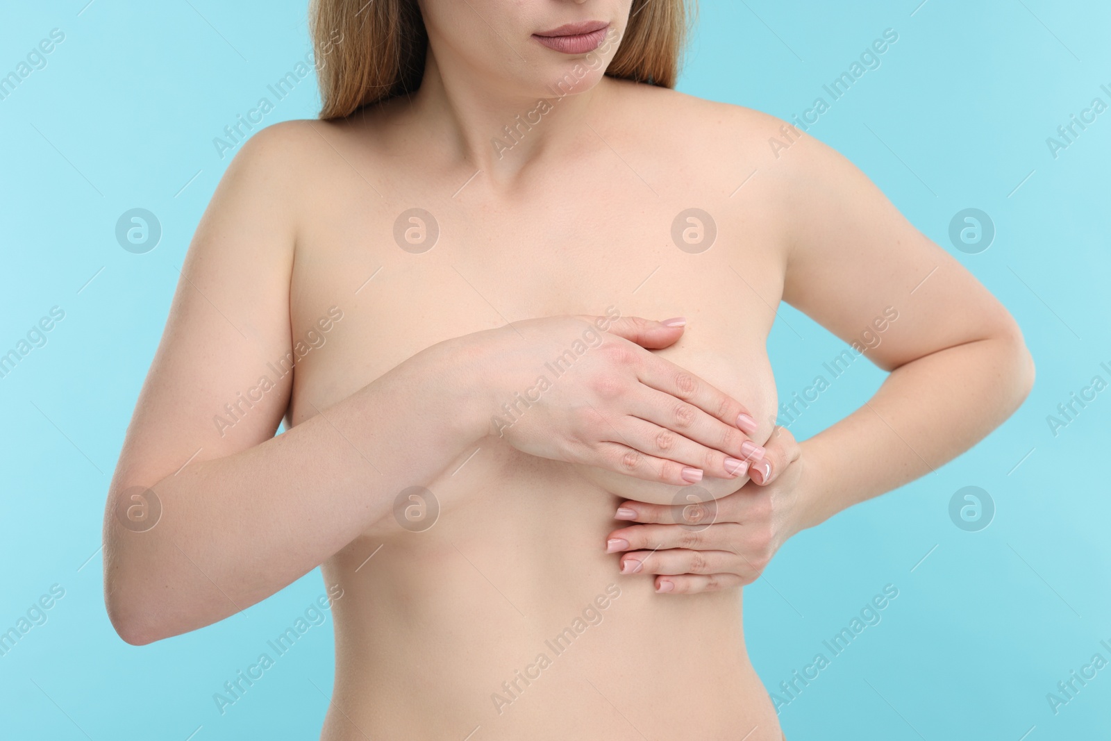 Photo of Mammology. Naked young woman doing breast self-examination on light blue background, closeup