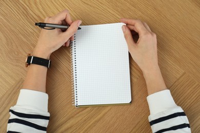 Photo of Left-handed woman writing in notebook at wooden table, top view
