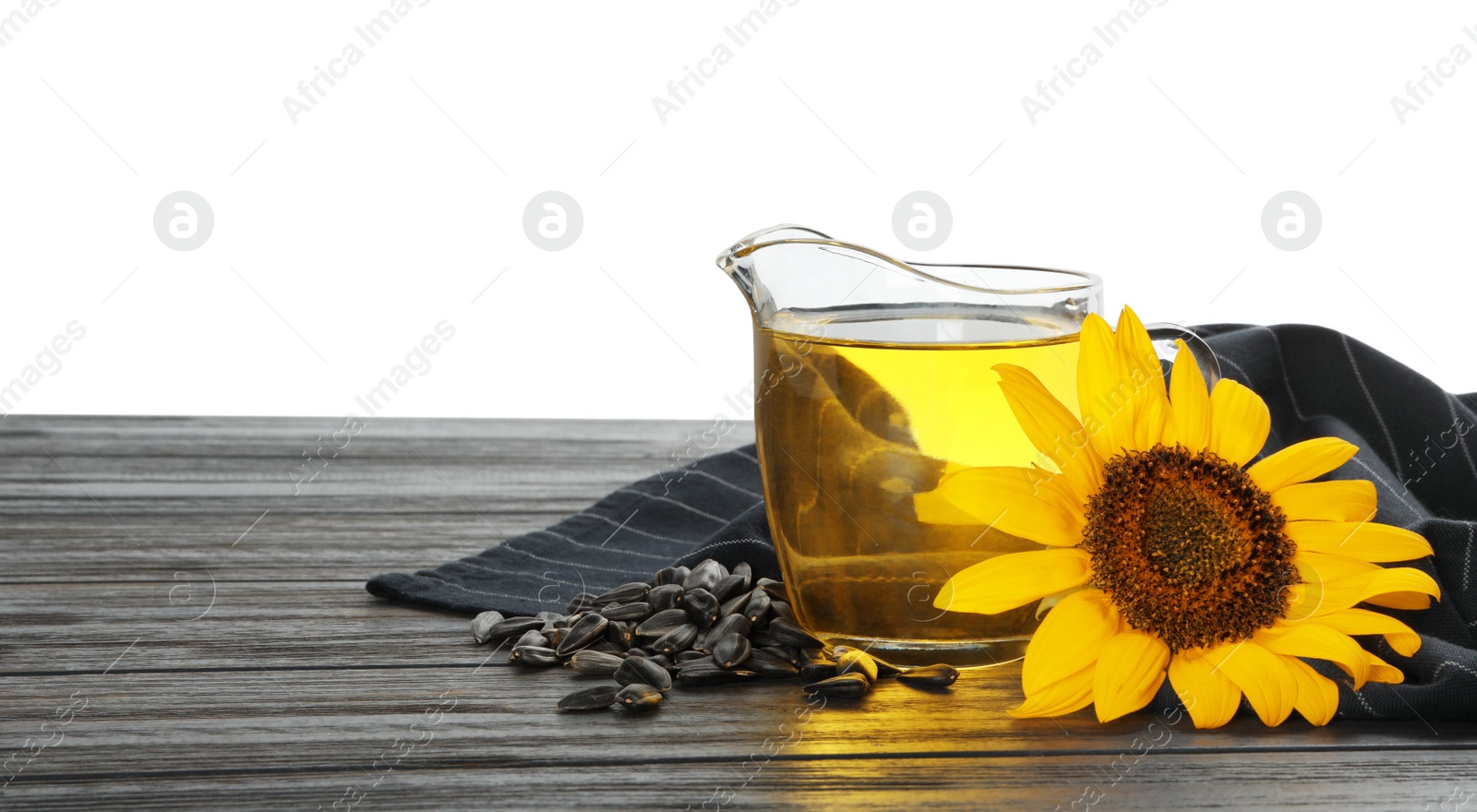 Photo of Sunflower, jug of oil and seeds on black wooden table against white background, space for text