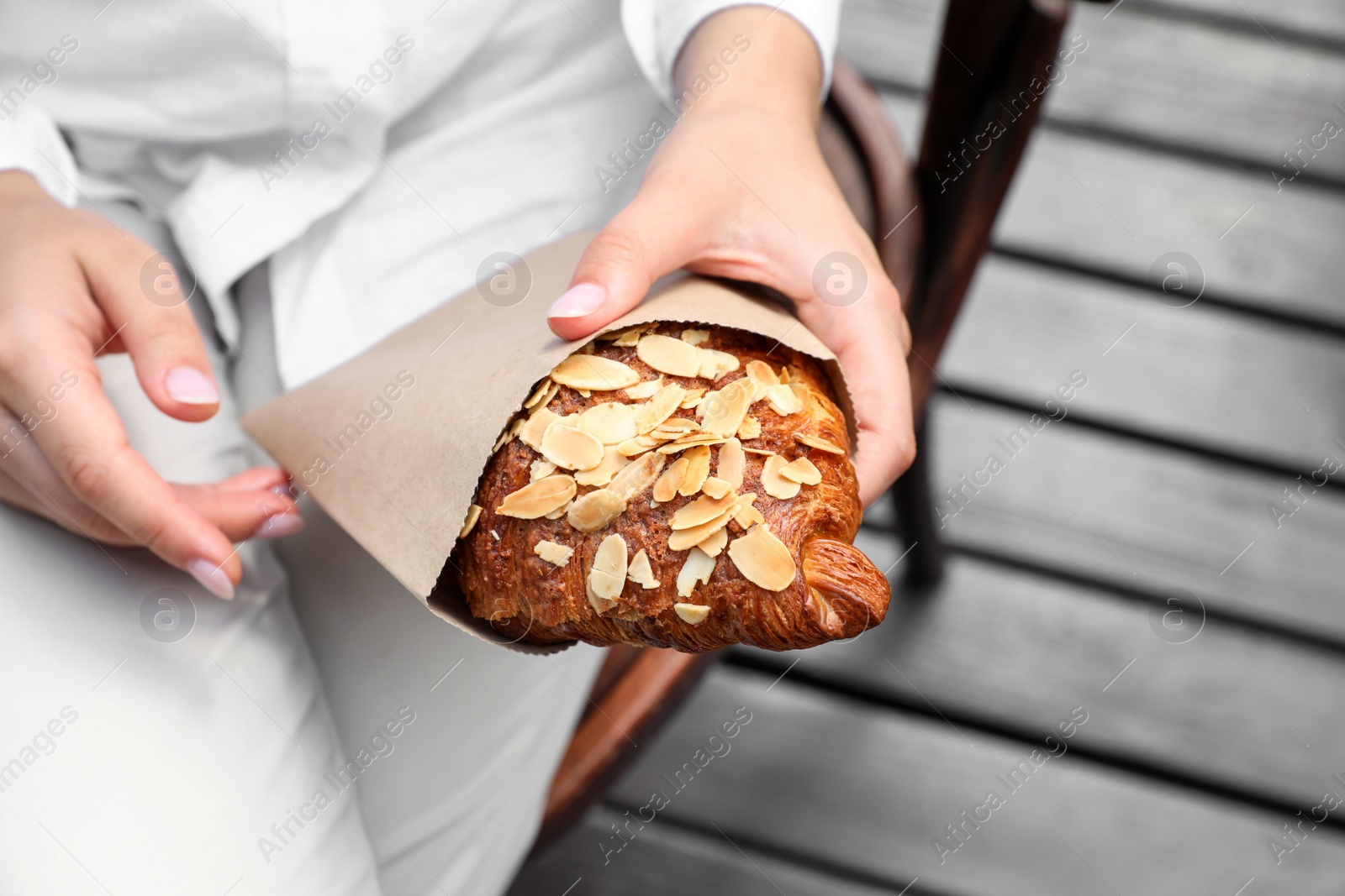 Photo of Woman with delicious croissant outdoors, closeup view