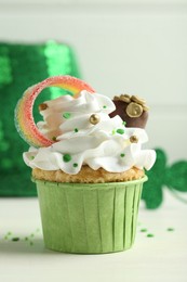 Photo of St. Patrick's day party. Tasty cupcake with sour rainbow belt and pot of gold toppers on white table, closeup