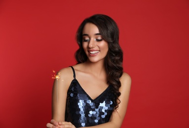 Photo of Beautiful young woman wearing elegant dress with sparkler on red background. Christmas party