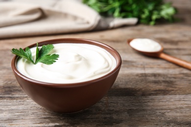 Photo of Bowl of fresh sour cream with parsley on wooden table