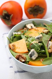 Photo of Tasty salad with persimmon, blue cheese and walnuts served on white table, closeup