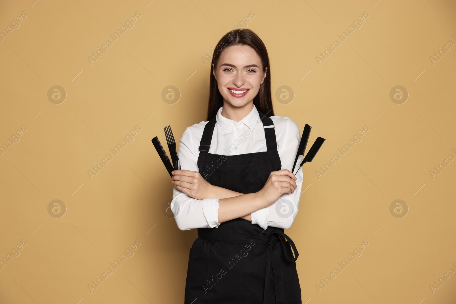 Photo of Portrait of happy hairdresser with combs on beige background