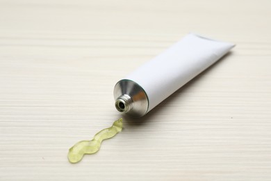 Photo of Open white tube with ointment on light wooden table