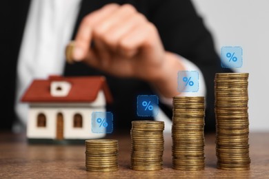 Mortgage rate. Woman putting coin into house shaped money box, closeup. Stacked coins and percent signs