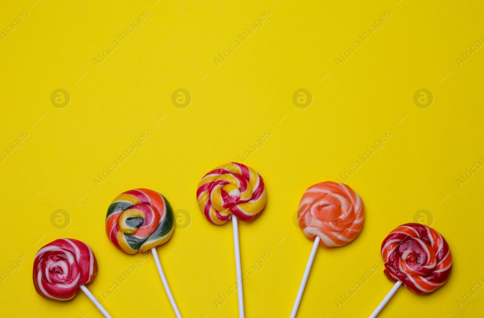 Photo of Delicious lollipops on yellow background, flat lay. Space for text
