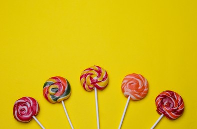 Delicious lollipops on yellow background, flat lay. Space for text