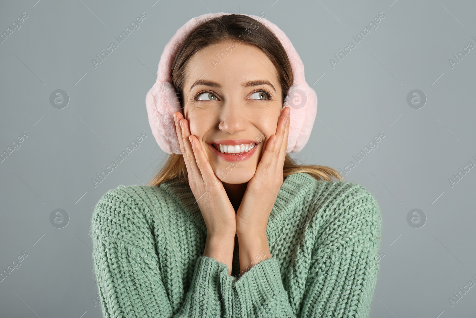 Photo of Happy woman wearing warm earmuffs on grey background