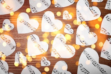 Christmas and New Year music. Hearts cut out from music sheets on wooden background, bokeh effect