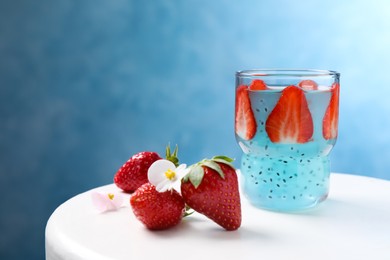 Photo of Light blue cocktail with strawberry and basil seeds on white table, space for text