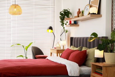 Photo of Stylish bedroom interior with comfortable bed, dressing table, lamps and green houseplants