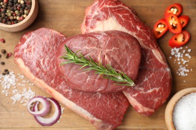 Photo of Pieces of raw beef meat and spices on wooden table, top view