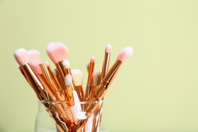 Photo of Jar with makeup brushes against color background. Space for text