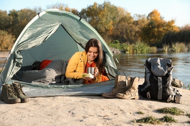 Young woman having breakfast in sleeping bag inside of camping tent