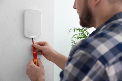 Photo of Man installing security alarm system on light wall at home, closeup